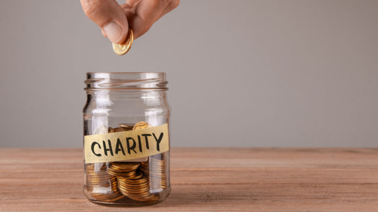 Charity. Glass jar with coins and an inscription charity. Man holds coin in his hand